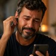 Um homem chorando ao ouvir algo no celular, com fones